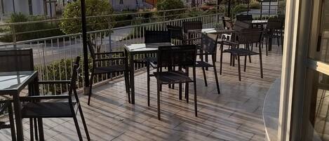 An outdoor seating area with tables and chairs, a street view, and a clear sky.