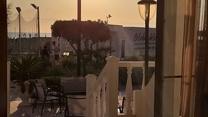 An outdoor patio area with a view of the sunset, a lamp post, and a building with a sign. - Hotel Ideal  (Rimini)
