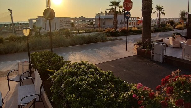 A sunset view with outdoor seating, palm trees, and a stop sign. - Hotel Ideal  (Rimini)