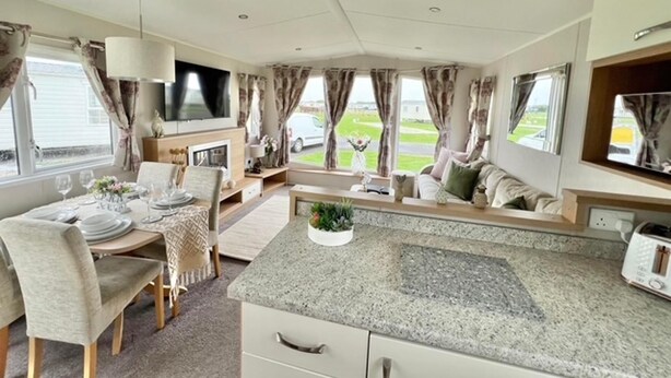 A modern RV interior with a dining area, seating, a kitchen with a granite countertop, and a television. - 3bed-8berth- Hot Tub-mablethorpe-pet Friendly-wifi (Mablethorpe)