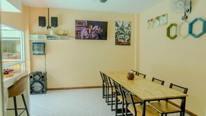 Ein Essbereich mit einem langen Holztisch und Stühlen, eine kleine Küchenzeile mit Kühlschrank und Spüle sowie ein Fenster, das natürliches Licht hereinlässt.