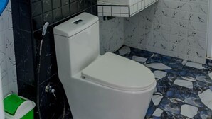 Ein Badezimmer mit Toilette, schwarzem Fliesenbelag, Waschbecken und Spiegel.
