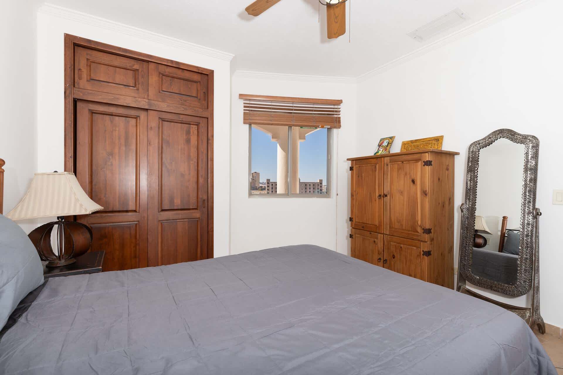 A bedroom with a large bed, wooden wardrobe, and a mirror.