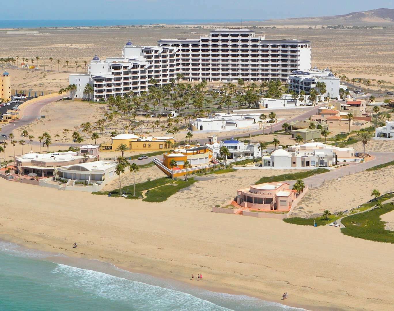 Een kustresort met een groot hotel, meerdere gebouwen en een zandstrand.