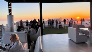 Un bar situé sur le toit, avec une terrasse et une vue sur le coucher de soleil au-dessus de la ville.