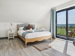 Ein Schlafzimmer mit einem großen Bett, einem Nachttisch, einer Lampe und Blick ins Freie.