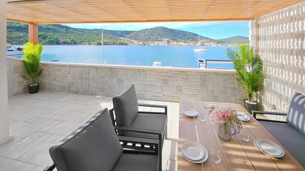A terrace with a stone wall, a wooden table set for dining, and two potted plants. - Beachfront Villa, Indoor Heated pool with Stunning view (Vinišce)