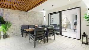 A modern patio area with a stone wall, a wooden ceiling, and a dining set. - Beachfront Villa, Indoor Heated pool with Stunning view (Vinišce)