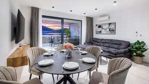 A modern living room with a dining area, a flat-screen TV mounted on the wall, a grey sofa, and a potted plant. - Beachfront Villa, Indoor Heated pool with Stunning view (Vinišce)