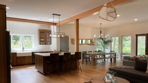 Una cocina moderna con una isla central, comedor con una mesa grande y sillas, y una sala de estar acogedora con un sofá y una mesita redonda.