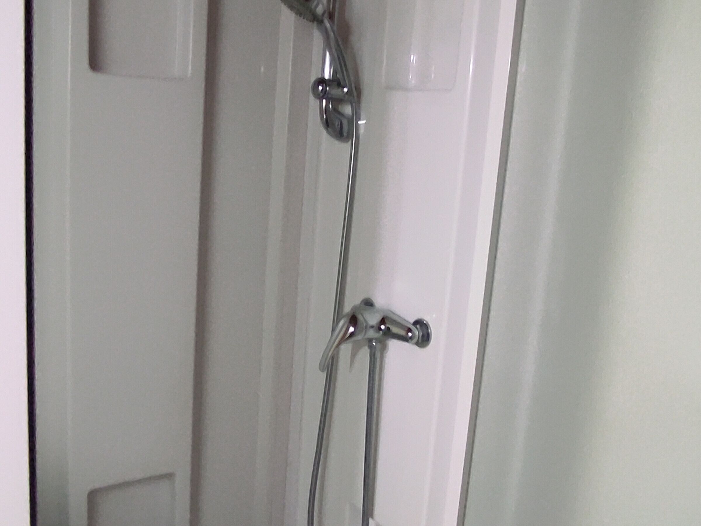 A shower with chrome fixtures and a white door.
