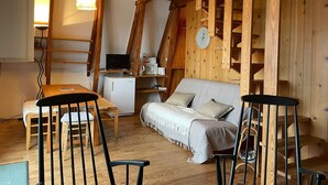 Interior acogedor de una cabaña con una mesa de comedor de madera, sillas, un sofá y una zona de cocina con microondas y un reloj.