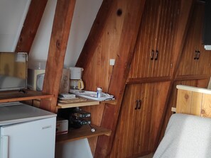 Une cuisine compacte avec des meubles de rangement en bois, un petit réfrigérateur, une machine à café et un four à micro-ondes.