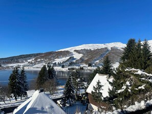 Un paysage enneigé avec un lac, des montagnes et un petit bâtiment doté d’un toit en pente.
