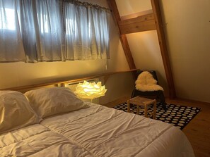 Une chambre à coucher avec un lit, une chaise, une lampe et une fenêtre avec des rideaux.