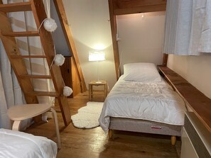 A compact bedroom with a bunk bed, a wooden ladder, a small table, and a lamp.