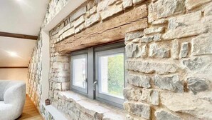 A room with a stone wall, a window with two doors, and a white chair. - Charming 4-Bedroom Cottage with Modern Comfort (Haroué)