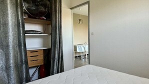 Un dormitorio con una cama, un armario y una zona de comedor visible a través de una puerta abierta.