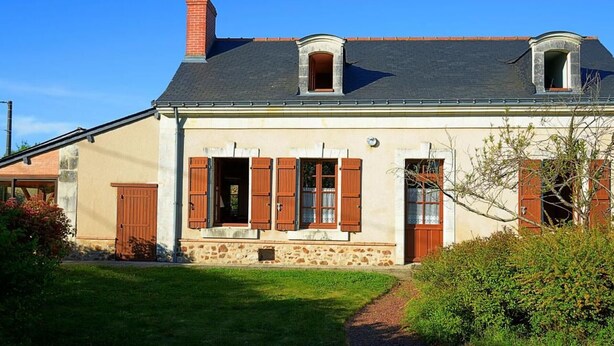 A two-story house with a stone facade, a chimney, and a small garden.