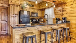 Une cuisine rustique, aménagée dans une cabane en bois, avec un îlot central, des tabourets de bar, un réfrigérateur, un four à micro-ondes et un évier.