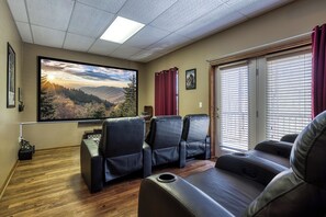 Habitación con un televisor de pantalla plana grande montado en la pared, asientos de cuero, piso de madera y una ventana con persianas.