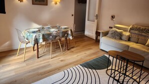 A dining area with a table set for four, two wall-mounted lamps, a framed picture, and a sofa with a throw blanket. - 2 rooms 4 pers 3* in Valloire, south, WiFi, parking, balcony (Valloire)