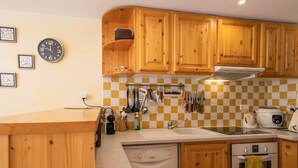 Une cuisine avec des meubles de rangement en bois, un crédence à carreaux, un évier, un lave-vaisselle et une cuisinière.