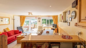 Un salon chaleureux avec un canapé rouge, une table à manger en bois et une vue sur l’extérieur grâce à de grandes fenêtres.