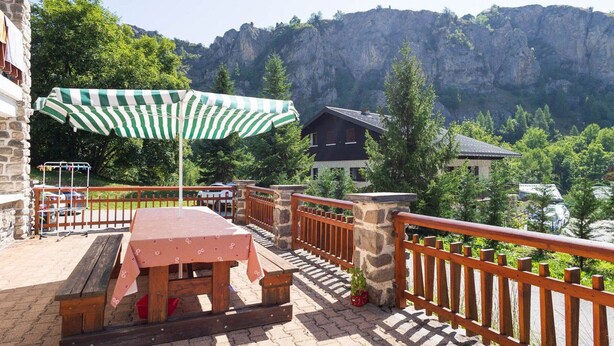 Une terrasse avec une table et un banc, un parasol à rayures et une vue sur une montagne.