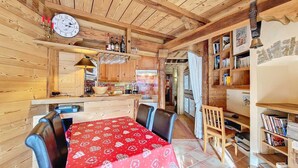 Un interior de madera con una mesa de comedor, sillas, una zona de cocina y una estantería.