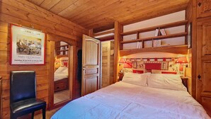 Una habitación de madera con una cama, una silla y estanterías llenas de libros.