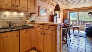 Interior de una cabaña de madera con cocina amueblada, alacenas de madera, un salpicadero de azulejos y comedor con mesa y sillas.
