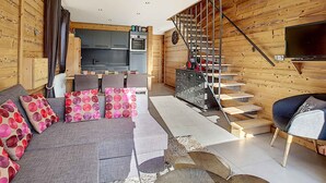 A modern living room with a sofa, a dining area, a kitchen, and a staircase leading to a loft. - Cozy apartment in La Clusaz, perfect for 6 guests, with 3 bedrooms (La Clusaz)