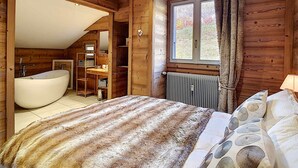 A log cabin bedroom with a large bathtub, a window with curtains, and a bed with patterned bedding. - Cozy apartment in La Clusaz, perfect for 6 guests, with 3 bedrooms (La Clusaz)
