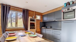 A modern kitchen with grey cabinets, a built-in oven, and a wooden dining table set with plates and glasses. - Cozy apartment in La Clusaz, perfect for 6 guests, with 3 bedrooms (La Clusaz)