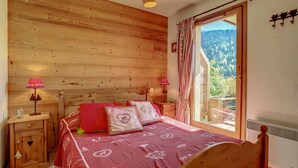Ein Schlafzimmer aus Holz mit einem Bett, zwei Nachttischen, einem Fenster mit Blick ins Freie und einer Deckenleuchte.
