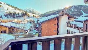 Un edificio de madera con balcón, rodeado de casas nevadas y montañas.
