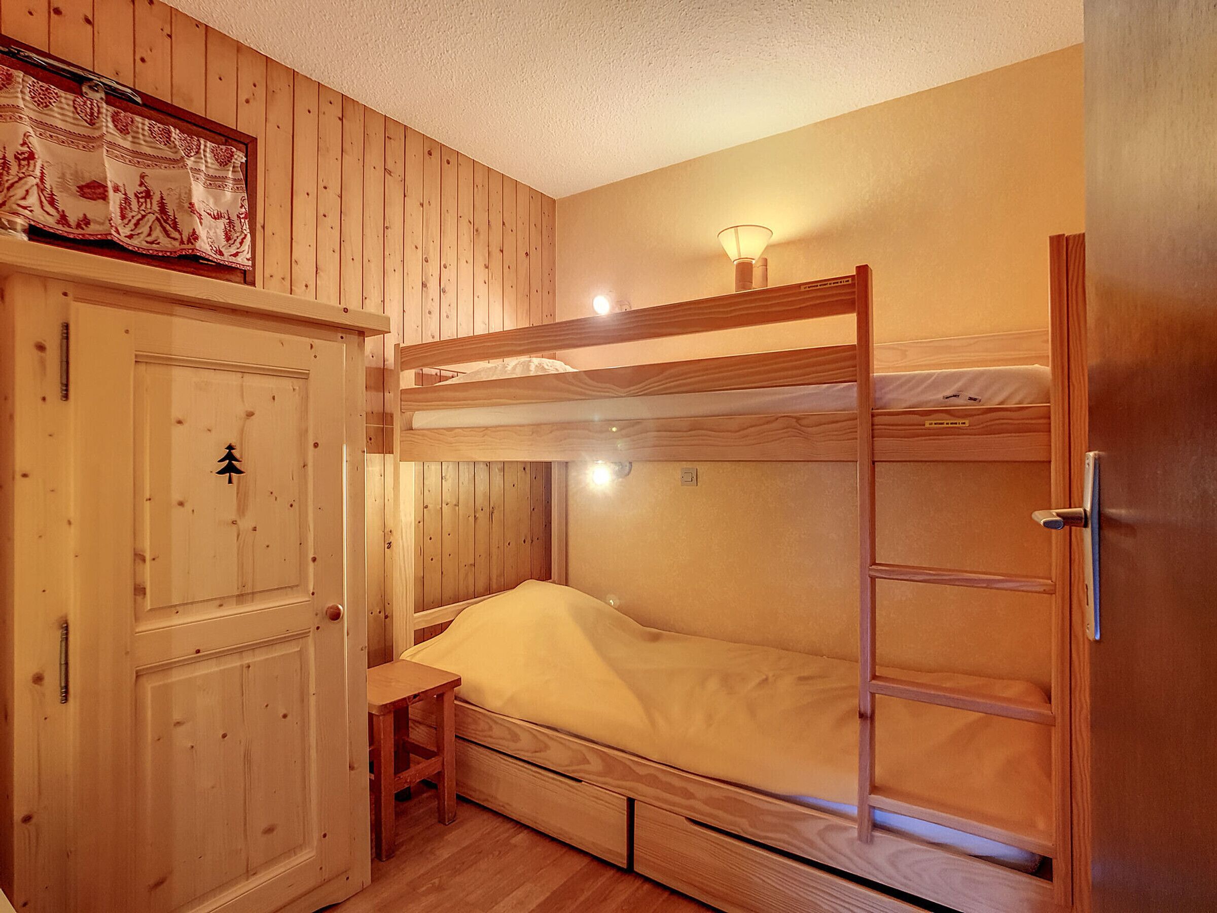 Ein Schlafraum mit Etagenbett, Holztür, kleinem Tisch und Nachttischlampe.