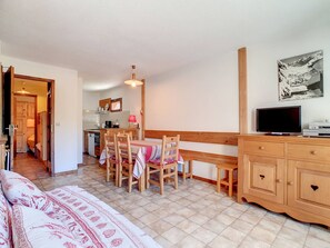 A cozy room with a bed, a wooden desk, a television, and a kitchen area in the background. - Apartment 40sqm, 6 people, south balcony, wifi included (La Clusaz)