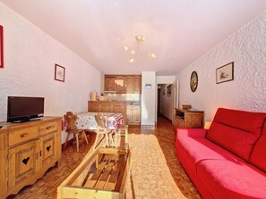 Uma sala de estar aconchegante com um sofá vermelho, móveis de madeira, uma televisão e uma cozinha ao fundo.