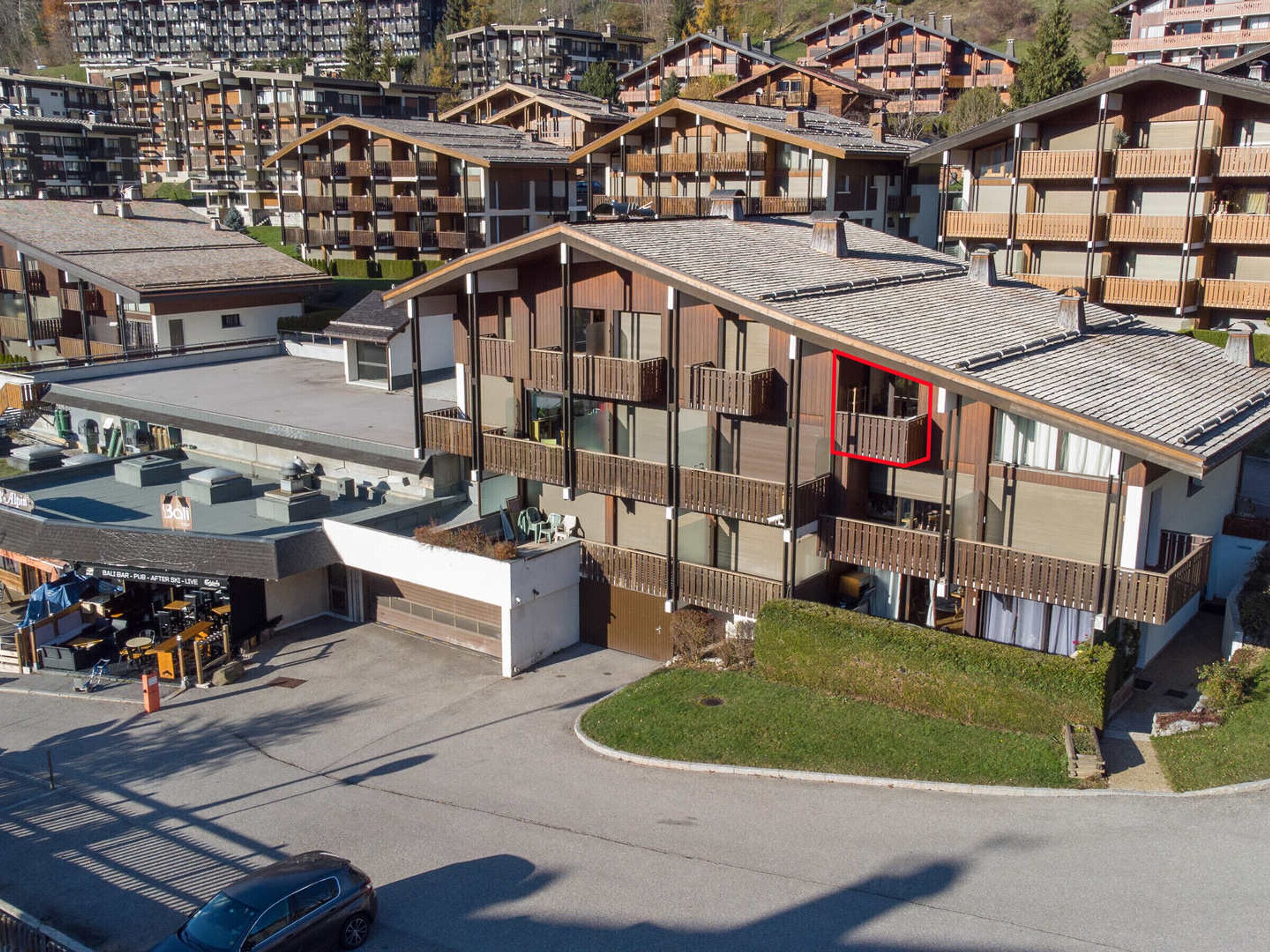 Un hotel de varios pisos con balcones, un telesilla y un área de estacionamiento.