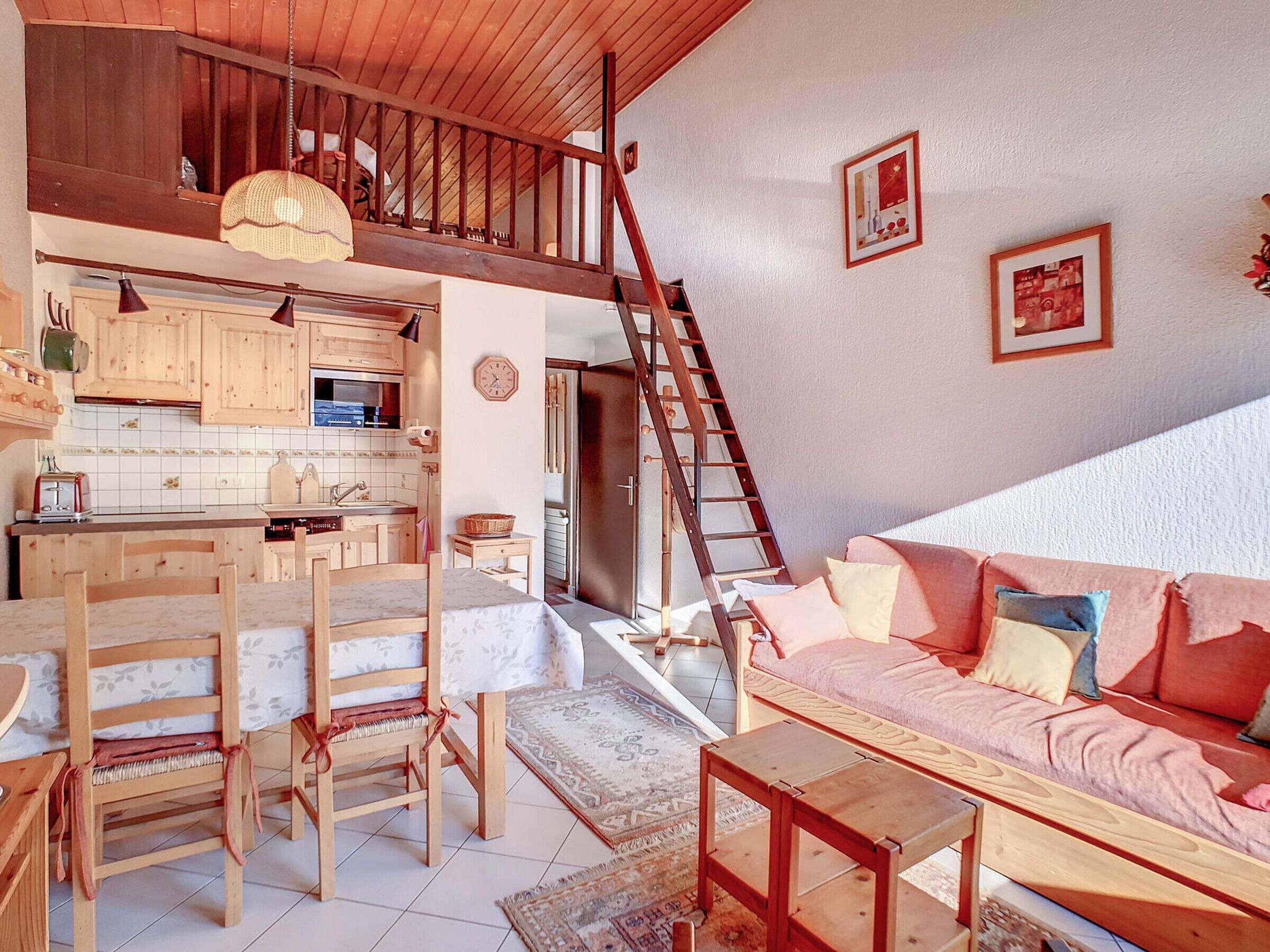Een ruime woonkamer met een houten trap, een keuken met houten kasten, een eettafel met stoelen en een bank met kussens.