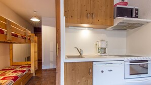 Eine kleine Küche mit Mikrowelle, Kaffeemaschine und kleinem Backofen. Daneben befindet sich ein Etagenbett mit einem gemusterten Bettbezug.