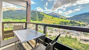 Un balcón con mesa y sillas que da a un paisaje montañoso con un pueblo abajo.