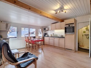 A cozy kitchen with wooden cabinets, a dining table with chairs, and a view of the snowy outdoors through the windows. - Cozy studio in La Clusaz for 4 people (La Clusaz)