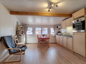 A cozy kitchen with wooden cabinets, a dining table with chairs, and a window with a view of a snowy landscape. - Cozy studio in La Clusaz for 4 people (La Clusaz)