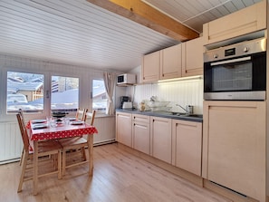 A cozy kitchen with wooden cabinets, a dining table with chairs, and a view of a snowy landscape through the windows. - Cozy studio in La Clusaz for 4 people (La Clusaz)