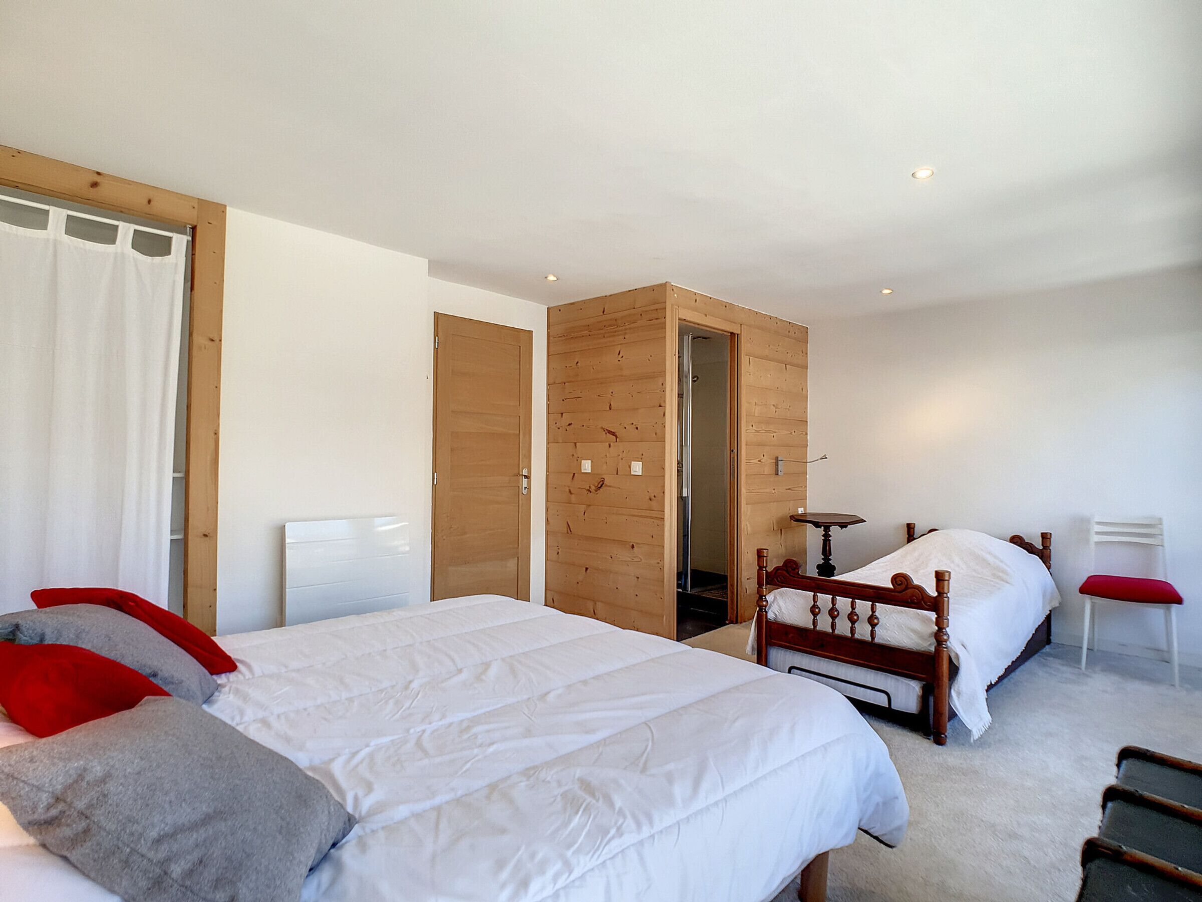 A bedroom with two beds, wooden wardrobes, a small table, and a chair.