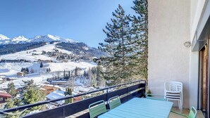 Ein Balkon mit Tisch und Stühlen mit Blick auf eine verschneite Berglandschaft.