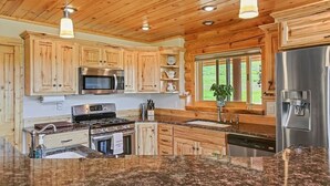 A kitchen with wooden cabinets, a stainless steel refrigerator, a microwave, a stove, granite countertops, and pendant lighting. - Warm River Butte Lodge (Ashton)